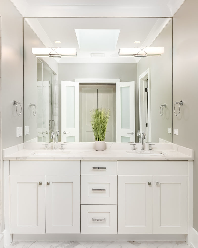 A modern bathroom with a white cabinet, a marble countertop, and lights mounted on the mirror.